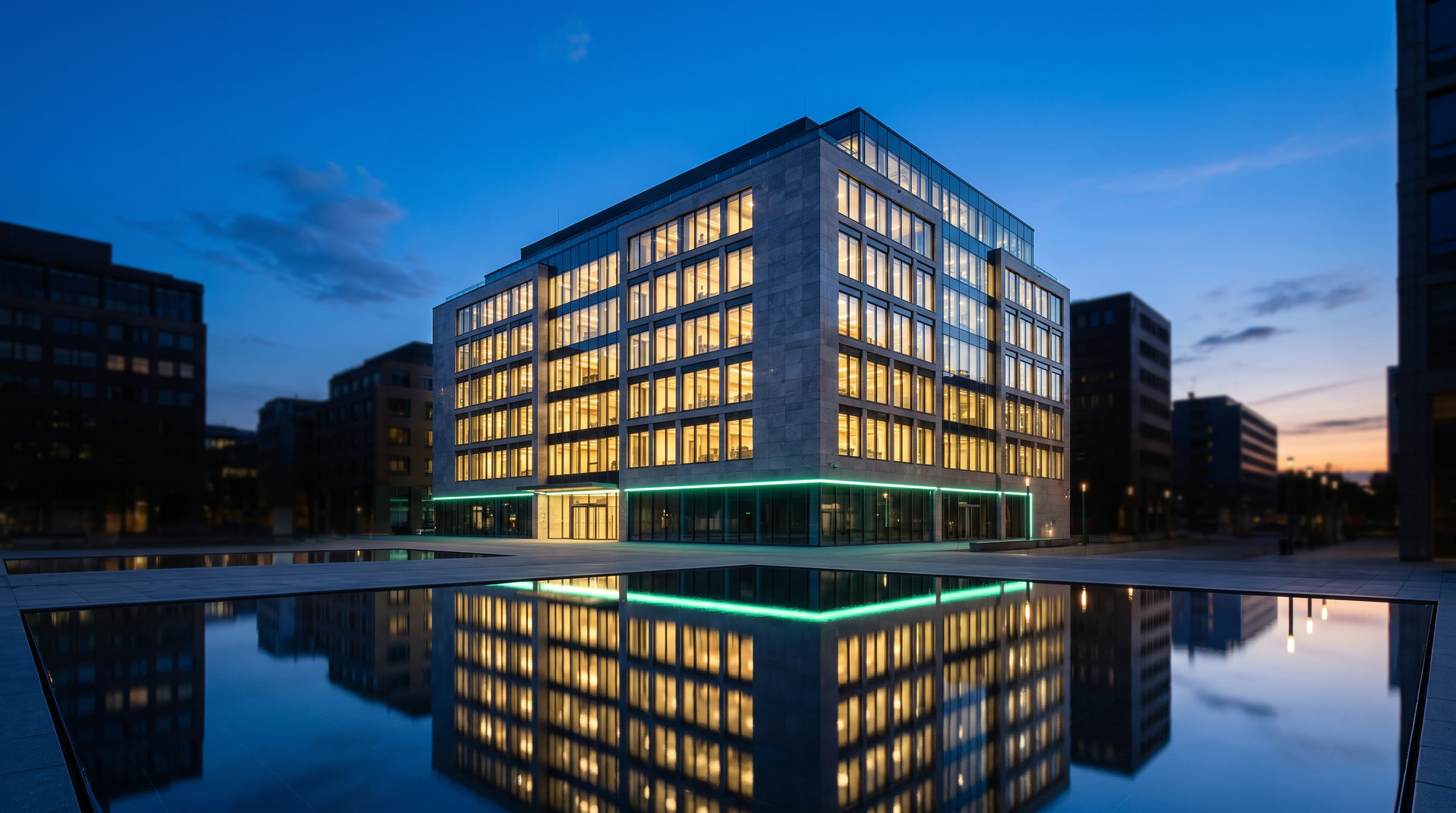 An OCOA-standard commercial office asset at dusk — floors warmly lit from within, a mint verification band tracing the base, mirrored in a still reflecting pool